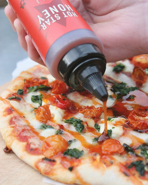 A bottle of Hot Star Honey being drizzled over hot pizza